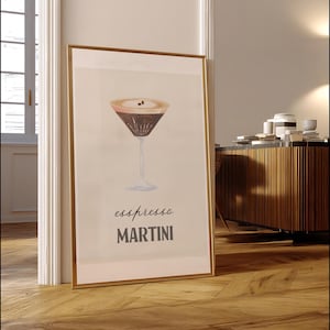 Op de afbeelding: Een ingelijste print met een espresso martini. Het kunstwerk toont een cocktail in aquarel-stijl in een klassiek martini glas. De woorden "espresso MARTINI" staan eronder in donkergrijs. De lijst is goudkleurig.