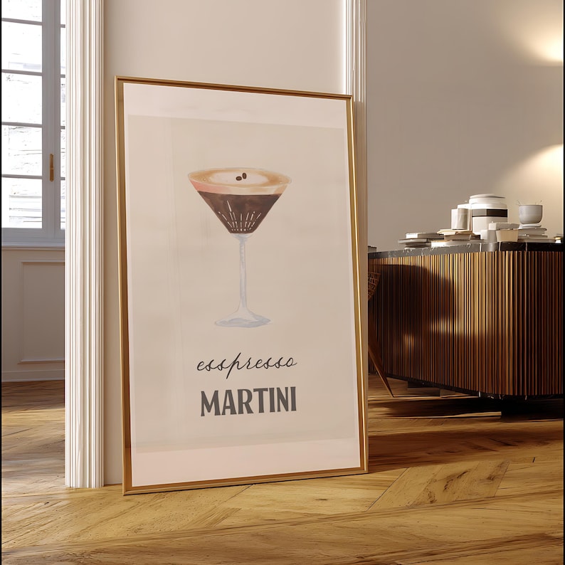Op de afbeelding: Een ingelijste print met een espresso martini. Het kunstwerk toont een cocktail in aquarel-stijl in een klassiek martini glas. De woorden "espresso MARTINI" staan eronder in donkergrijs. De lijst is goudkleurig.