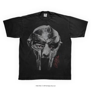 May include: Black t-shirt with a grayscale image of a metal mask and visible eyes. A red signature is below the mask. The shirt has a crew neck and short sleeves. The text "YIVEZ TEES © 2019 All Rights Reserved" is at the bottom.