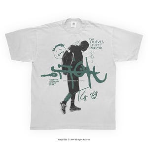 Puede incluir: Camiseta blanca con un diseño gráfico en verde y negro. El diseño incluye una figura, el texto "THE TRAVIS SCOTT TAKEOVER" y "UTOPIA". El texto adicional incluye "CREATOR VISIONARY OF THE YEAR". La camiseta tiene mangas cortas.