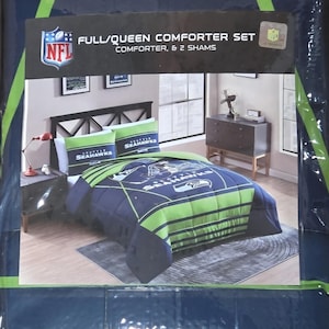 May include: Full/Queen comforter set in a package. The set includes a comforter and two shams. The comforter and shams feature a navy blue and green color scheme with the Seattle Seahawks logo and team name. The packaging also displays the NFL logo.