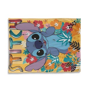 May include: A yellow blanket featuring the character Stitch from Lilo & Stitch, surrounded by colorful tropical flowers. The blanket has the word "Stitch" in a playful font on the left side. The blanket is a soft, cozy item.