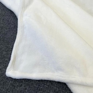 May include: A close-up shot of a soft, white blanket. The blanket is folded, revealing a plush texture and a smooth, finished edge. The fabric appears to be a cozy, warm material, perfect for snuggling. The blanket is a solid, bright white color.