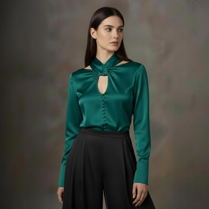 Puede incluir: Blusa de sat&eacute;n verde esmeralda con mangas largas y cuello con abertura. La blusa tiene una botonadura frontal y se combina con pantalones negros de pernera ancha. La tela tiene un brillo sutil, lo que sugiere un estilo formal o elegante.