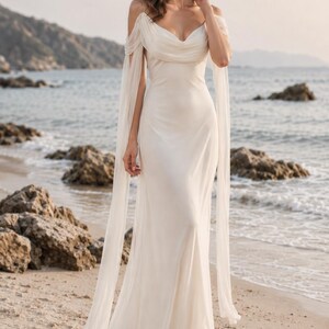 May include: A floor-length off-white gown featuring a draped cowl neckline, thin spaghetti straps, and long, flowing sheer fabric sleeves that extend from the shoulders. The dress has a fitted bodice and a floor-length skirt with a soft, fluid drape.