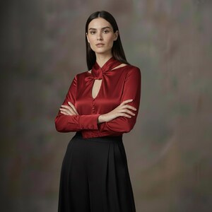 Puede incluir: Una mujer con una blusa de sat&eacute;n roja con cuello de ojo de cerradura y mangas largas, combinada con pantalones negros de pernera ancha. La mujer tiene los brazos cruzados.