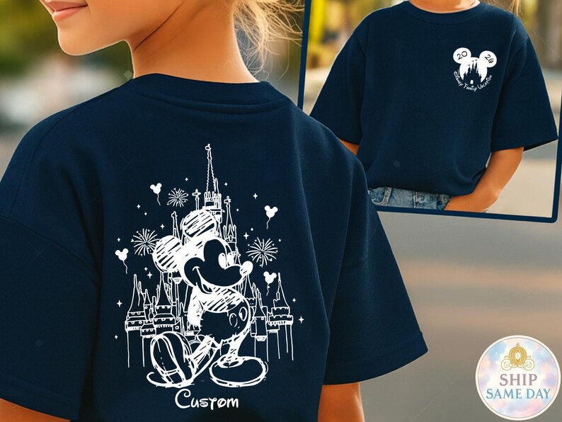 May include: Navy blue t-shirt featuring a white graphic of Mickey Mouse in front of a castle, with fireworks and the word "Custom" below. The shirt also has a small Mickey Mouse head logo with text on the front.