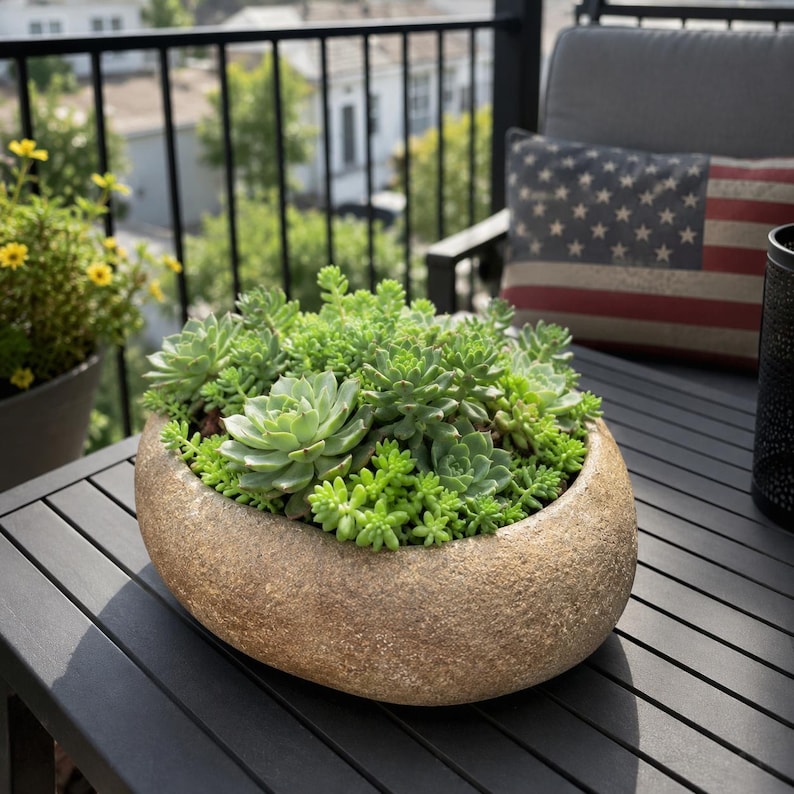 May include: A round, textured, tan stone-like planter filled with a dense arrangement of various green succulent plants. The planter has a smooth, curved rim and a rough, porous exterior surface, housing multiple types of small, fleshy succulents.