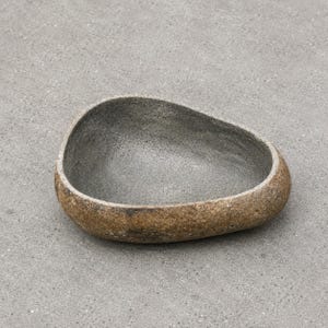 May include: A bowl with an irregular, organic shape resembling a river stone. The exterior has a textured, mottled brown and tan finish, while the interior features a smooth, speckled dark gray surface with a deep, concave basin design.