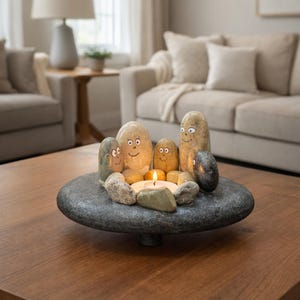 May include: A decorative stone candle holder with a lit candle surrounded by painted stones with faces. The candle holder is on a dark wooden table in a living room setting. The stones are various sizes and colors.
