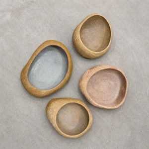 May include: Four organic-shaped bowls with textured, golden-brown outer surfaces. One bowl features a smooth, light gray interior, while the other three bowls have textured, earthy-toned interiors in shades of tan, beige, and light brown.
