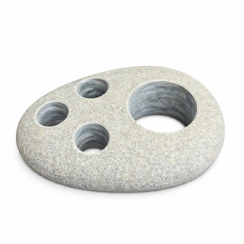 May include: A gray stone toothbrush holder with four circular openings. The holder has a smooth, rounded shape and a speckled texture. The openings are of varying sizes, designed to hold toothbrushes and other bathroom accessories.