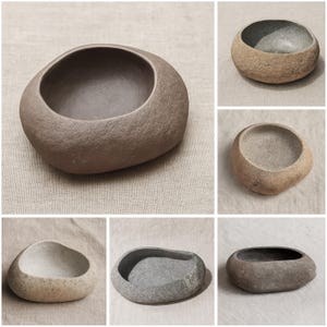 May include: A collection of stone-like bowls in various shades of gray and brown. The bowls have a smooth, rounded shape with a deep interior, perfect for holding small items. The natural, organic design adds a touch of rustic elegance to any space.