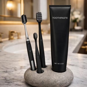 Può includere: Un tubetto di dentifricio nero e tre spazzolini neri sono esposti in un porta spazzolini di pietra grigia. Il tubetto di dentifricio ha la scritta "TOOTHPASTE" e l'etichetta "NET WT. 6 OZ."