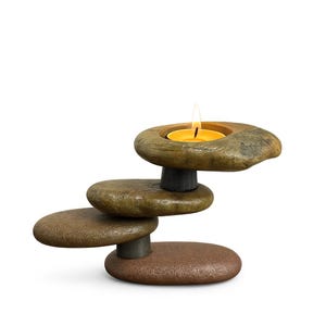 Pode incluir: Um castiçal de pedra empilhada com uma vela amarela acesa. O suporte é feito de quatro pedras planas de aparência natural em tons de castanho e cinza, sustentadas por pequenos cilindros cinza escuro.