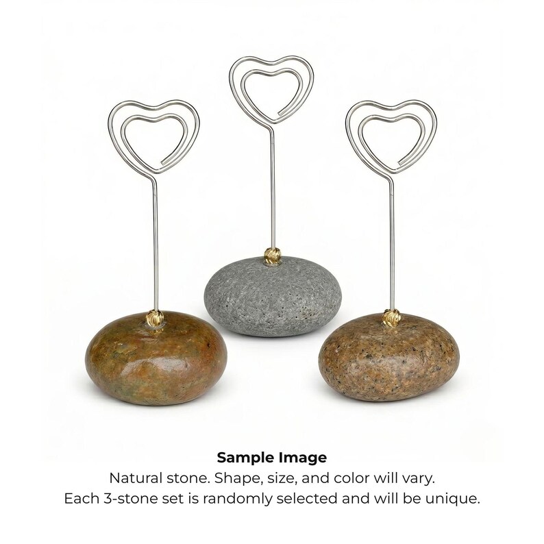 May include: Three natural stone card holders. Each holder features a silver-colored wire heart design attached to a stone base. The stones vary in color, including brown and gray, and have a small gold-colored accent.