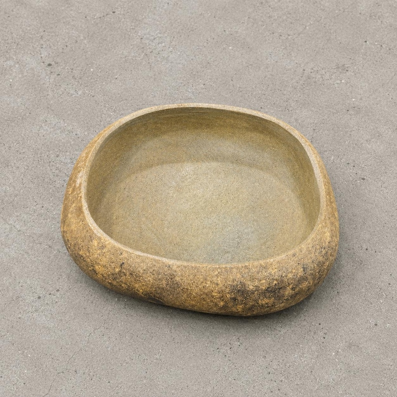 May include: A low, wide, rounded ceramic bowl with an irregular, organic shape. The exterior features a textured, mottled finish in shades of earthy brown and tan, while the interior has a smoother, lighter beige surface with visible brush strokes.