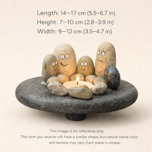 May include: A stone candle holder with a gray, round base and a collection of smooth, painted stones. The stones have faces and surround a lit candle. The length is 5.5-6.7 inches, height is 2.8-3.9 inches, and width is 3.5-4.7 inches.