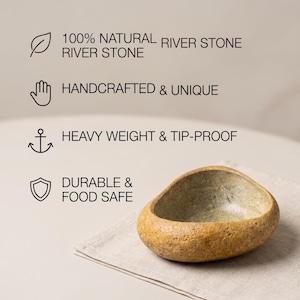 May include: A natural river stone bowl with a unique, handcrafted design. The bowl is a light brown color with a textured surface and a smooth interior. The text in the image says it is durable and food safe.