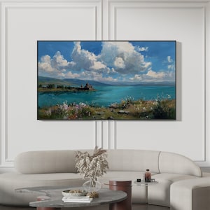 May include: A framed landscape painting depicts a serene lake scene under a bright blue sky filled with fluffy white clouds. The artwork features a castle on a small island, with colorful wildflowers in the foreground. The painting is displayed above a modern sofa.