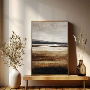 May include: Abstract landscape painting in a gold frame. The artwork features a neutral color palette with shades of brown, beige, and black, depicting a serene landscape. The painting is displayed on a wooden bench with decorative vases.