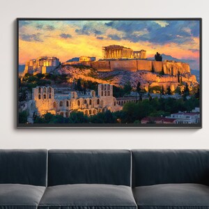 May include: Framed print of the Acropolis in Athens, Greece, at sunset. The image features the Parthenon and other ancient structures bathed in warm, golden light against a colorful sky. The artwork is displayed above a dark gray sofa.