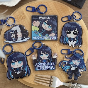 Könnte beinhalten: Sechs Acryl-Schlüsselanhänger mit Anime-Figuren mit dunkelblauem Haar und blauen Akzenten. Zwei quadratische Anhänger zeigen den Text "WORLD ADOMINATION" und "ADOSOLUTE CINEMA". Die anderen zeigen Charaktere in verschiedenen Posen, alle an dunkelblauen Kunststoffverschlüssen befestigt.