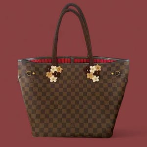 Puede incluir: Bolso tote a cuadros marrones y beige con asas marrones y adornos florales. El bolso tiene un interior rojo y herrajes dorados. Un accesorio elegante.