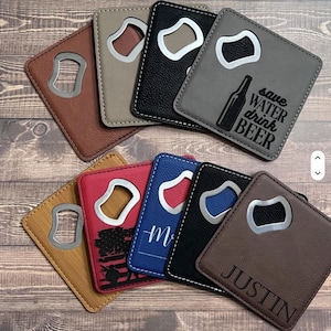 May include: A collection of leatherette bottle openers in various colors, including brown, tan, black, red, blue, and gray. Each opener has a silver-colored metal opener. Some have text or designs, such as "Save Water Drink Beer" and the name "Justin."