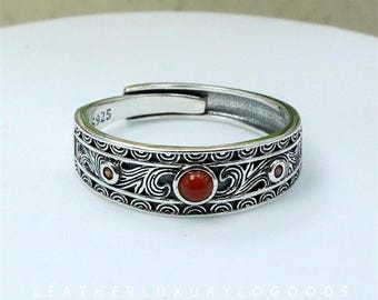 May include: Adjustable sterling silver ring with an engraved band. The ring features three red-orange gemstones. The text "S925" is visible on the band. A handcrafted piece of jewellery.