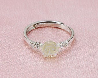 May include: A silver adjustable ring featuring a light yellow rose-shaped gemstone. The ring has small clear stones either side of the rose. The background is a light pink fabric. The text "LEATHERLUXURYLOGODS Handcrafted Jewellery" is at the bottom.