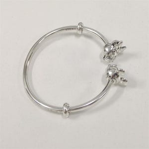 May include: A silver bracelet featuring two Mickey Mouse charm details. The bracelet is made of a shiny metal and has a simple, elegant design. The charms are detailed and add a playful touch to the jewellery.