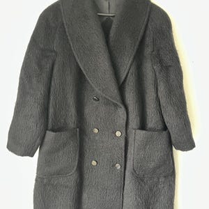 Könnte beinhalten: Ein schwarzer, doppelreihiger Mantel mit breitem Kragen und zwei Vordertaschen. Der Mantel ist aus einem flauschigen Material gefertigt und hängt an einem schwarzen Kleiderbügel.