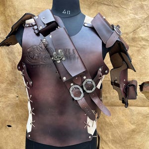 May include: A brown leather chest armour with shoulder pauldrons, a belt, and a holster. The armour has silver buckles and rivets. The text "Lord Of Orcs" is visible on the chest.