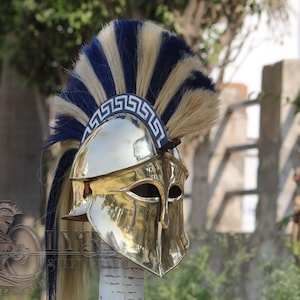 May include: A polished brass Spartan helmet with a blue and beige plume. The helmet has eye slits and a decorative band around the brow. The plume has alternating blue and beige stripes.