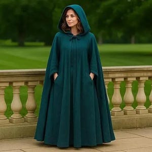 May include: A floor-length, dark teal hooded cloak featuring a structured hood, a simple tie closure at the neck, and two deep side pockets. The garment is made of a solid-colored fabric and drapes fully to the ground in a wide, flowing silhouette.