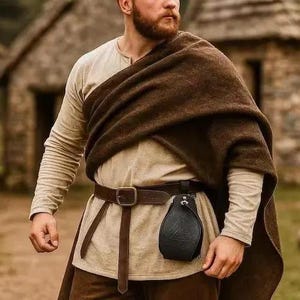 May include: A beige long-sleeved tunic paired with a dark brown wool cloak draped over one shoulder. A dark brown leather belt is worn around the waist, featuring a small black leather pouch attached to the side with a metal buckle and strap.