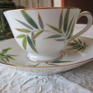 May include: A white teacup and saucer set with a gold rim and a green bamboo leaf design.
