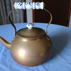 May include: A copper tea kettle with a white porcelain handle and lid decorated with blue floral designs.