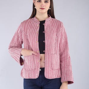 May include: A red and white striped jacket with a mandarin collar and two front pockets. The jacket has a button-up front and long sleeves. The model is wearing a black top and blue jeans.