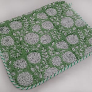 May include: A green quilted potholder with a floral design. It features white flowers and leaves on a green background. The edges are trimmed with a white and green striped fabric.