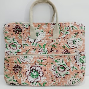 Puede incluir: Un bolso tote acolchado con un estampado floral en tonos melocotón, blanco, verde y burdeos. El bolso tiene un cierre de cremallera y asas de color crema. El bolso es rectangular y tiene una textura acolchada.
