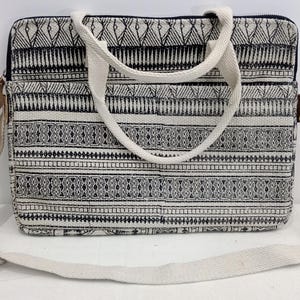 Op de afbeelding: Een rechthoekige laptoptas met een crèmekleurige canvas riem en handvatten. De tas heeft een zwart-wit geometrisch patroon. De tas heeft een ritssluiting en een crèmekleurige verstelbare schouderriem. De tas heeft een rechthoekige vorm.