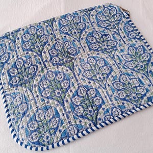 May include: A quilted laptop sleeve with a blue and white floral pattern. The sleeve has a zipper closure and a striped border in blue and white. The design features a repeating pattern of stylized leaves and flowers.