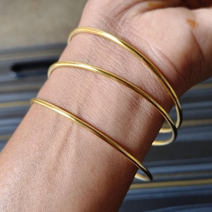 Peut inclure: Trois bracelets dorés sont portés au poignet. Les bracelets sont fins et ronds, avec une finition lisse et brillante. Le teint est brun clair. L'arrière-plan est flou.