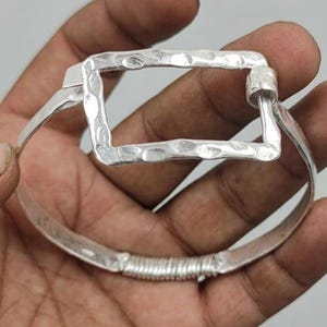 Peut inclure: Un bracelet en argent avec une pièce maîtresse rectangulaire martelée. Le bracelet a un design simple et élégant avec un détail en fil enroulé près du fermoir. Le métal a une finition légèrement texturée.