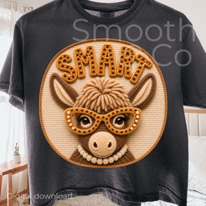 Op de afbeelding: Donkergrijs T-shirt met een cirkelvormig ontwerp met een gehaakte ezel met een bril en het woord "SMART" in bruine letters. De ezel heeft een bruine manen en oren, en de bril is versierd met kleine witte kralen. Het shirt heeft een ronde hals.