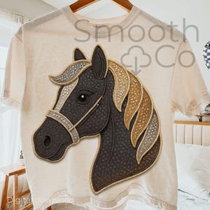 Op de afbeelding: Crèmekleurig T-shirt met een gedetailleerd paardenhoofd ontwerp. Het paard heeft een donkergrijs gezicht, een bruin en zilveren manen en een decoratieve teugel. De tekst "Smooth Co" is zichtbaar op het shirt.