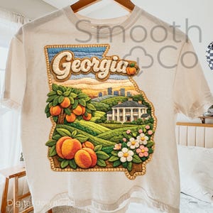 May include: Cream-colored t-shirt featuring a detailed embroidered design of the state of Georgia. The design includes the word "Georgia", peaches, a landscape with a house, and flowers. The shirt is a digital download.
