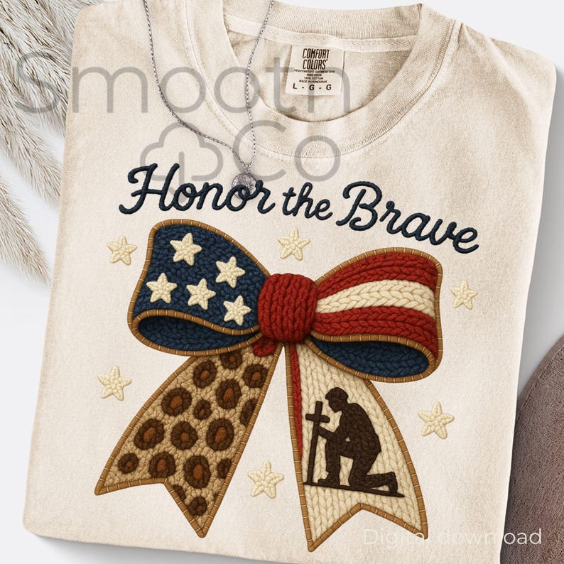 Puede incluir: Camiseta color crema con la frase "Honor the Brave" en escritura azul marino. El dise&ntilde;o presenta un lazo patri&oacute;tico con estrellas, rayas y una secci&oacute;n con estampado de leopardo, junto con un soldado arrodillado sosteniendo una cruz. La camiseta tiene una etiqueta Comfort Colors.